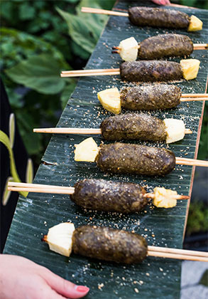 Heritage pork sausage with pineapple skewer on a banana leaf lined platter